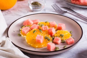 Fruit salad of watermelon, orange and pumpkin seeds on a plate on the table. Healthy food.